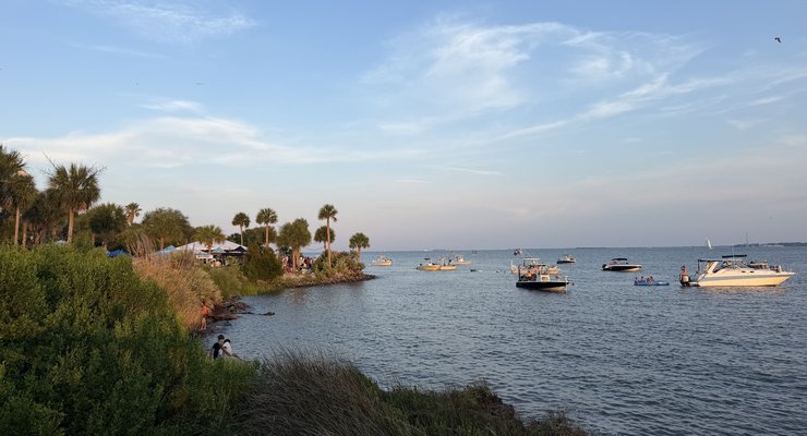Boats anchored in Charleston Harbor with palm trees and the Party at the Point concert crowd visible on shore, Mount Pleasant SC