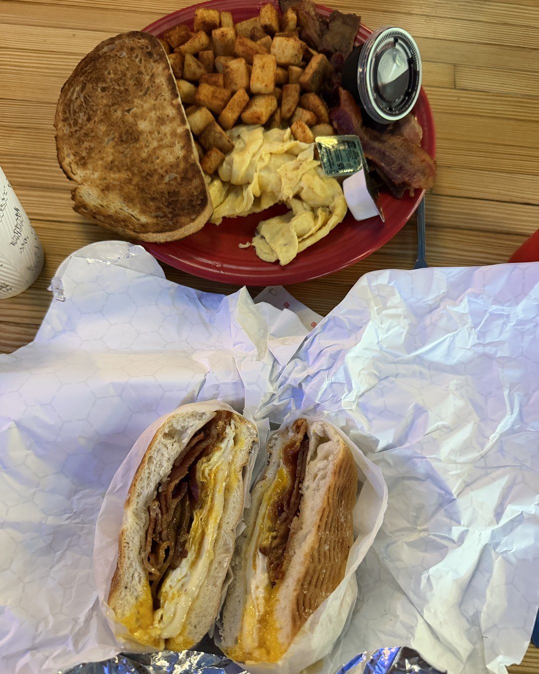 Bacon, egg and cheese breakfast sandwich cut in half next to a platter of scrambled eggs, home fries, bacon and toast