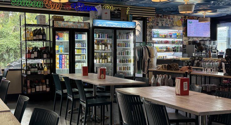 Indoor seating at Bodega with drink coolers, a neon bacon egg and cheese sign and a TV screen