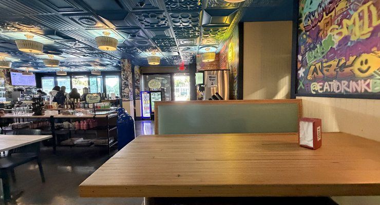 Bright graffiti mural and a wooden table inside Bodega with a tin ceiling and open dining room