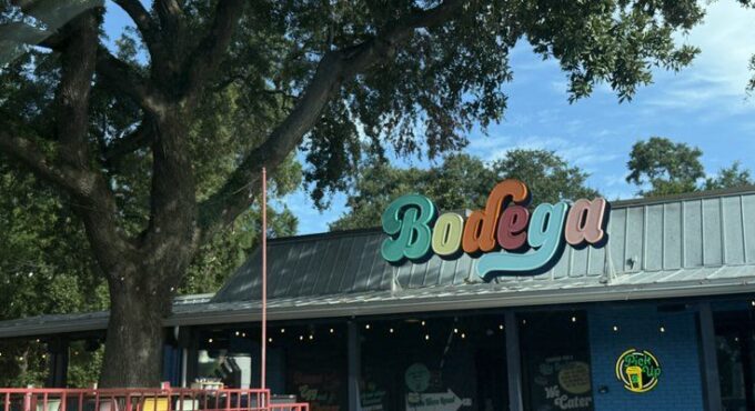 Colorful Bodega restaurant sign above a covered patio under a large oak tree