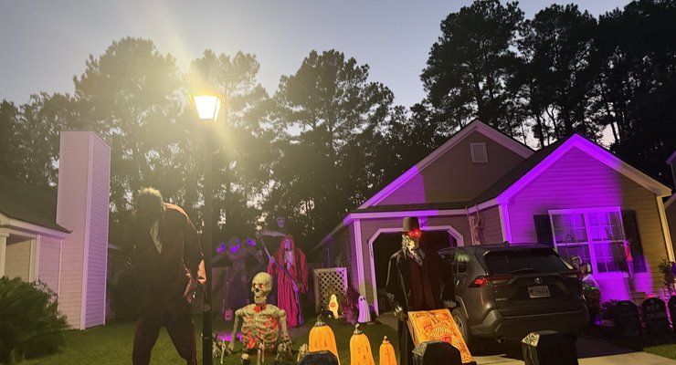 Halloween yard with glowing pumpkins, a skeleton and creepy figures beside a house with purple lights near Clements Ferry Road in Charleston, SC