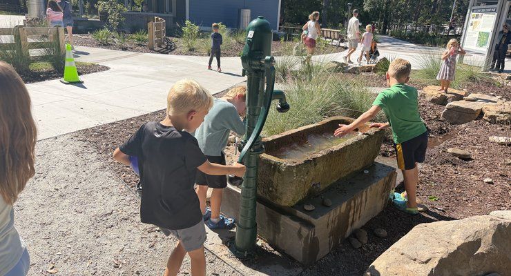 Children using a green hand pump and stone trough water feature at Old Towne Creek County Park