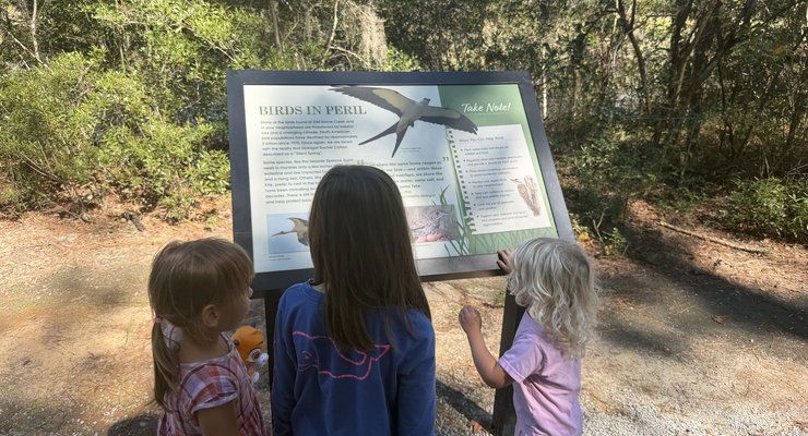 Three young children reading an interpretive sign about birds along the trail at Old Towne Creek County Park
