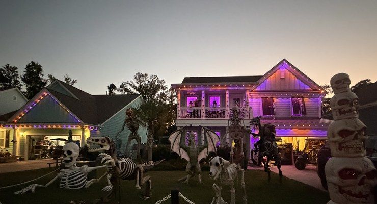 Giant skeletons and a bone dragon in a front yard lit with purple lights at dusk near Clements Ferry Road in Charleston, SC