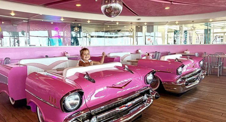 Little girl sitting in a pink Cadillac booth under a disco ball at Pinky's on the Beach