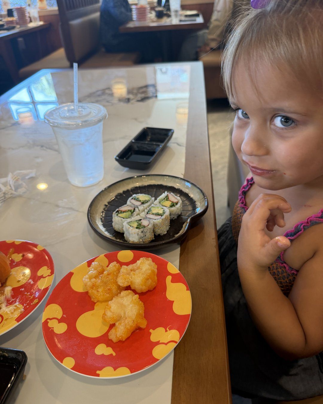 California roll and plates of food on the table at Revolving Sushi Kingdom with a child looking on