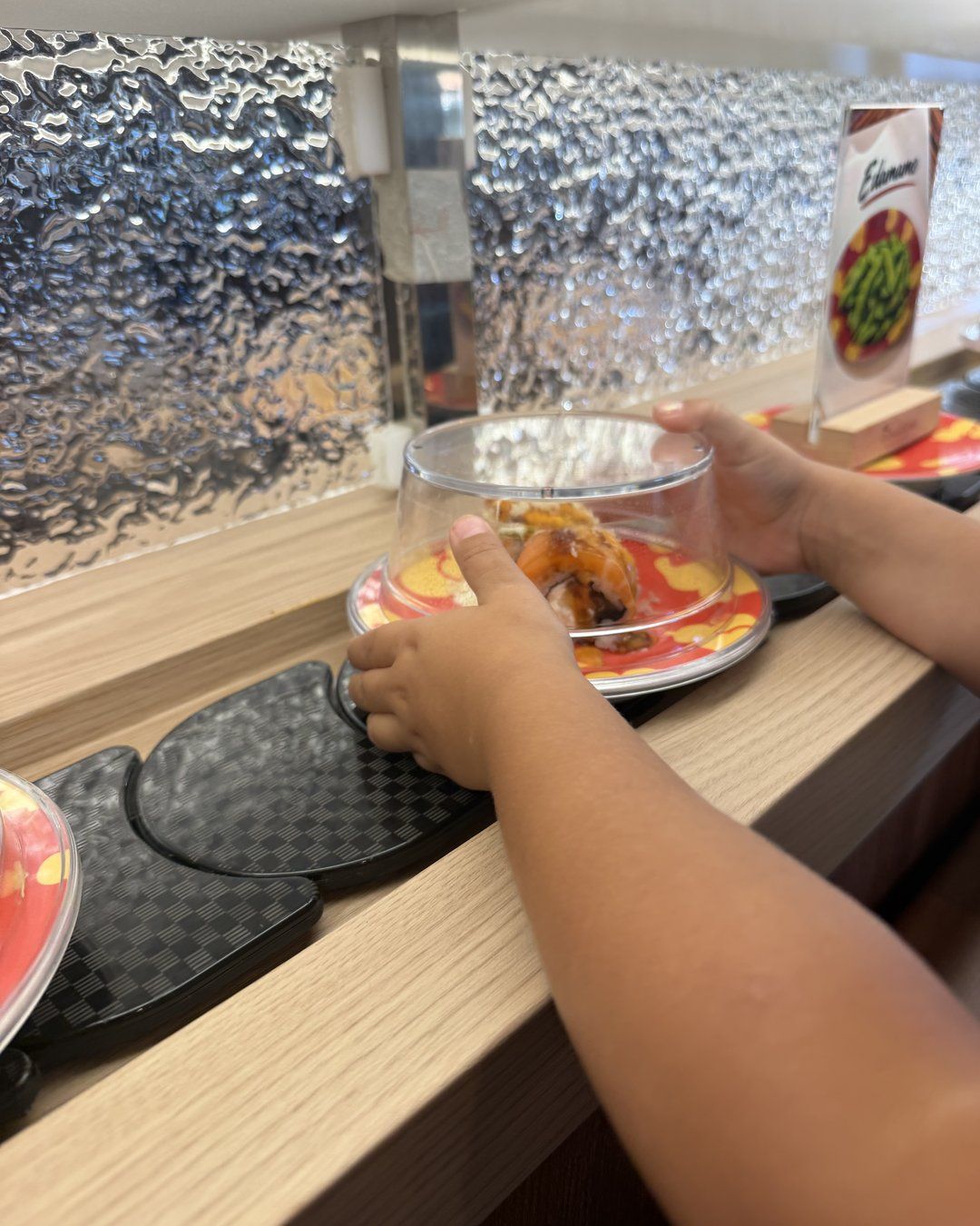 Child reaching for a plate on the sushi conveyor belt at Revolving Sushi Kingdom
