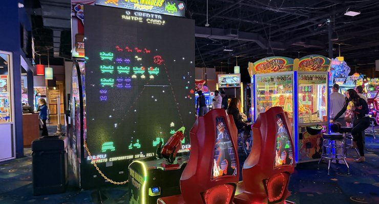 Arcade floor with a giant Space Invaders style screen and prize machines at Stars and Strikes in Summerville, SC