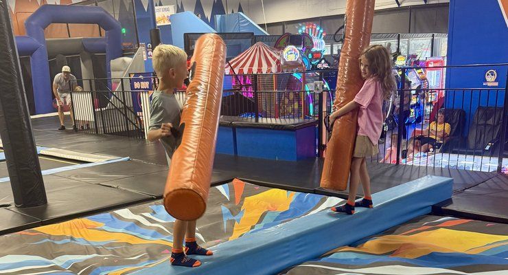 Two kids holding foam poles on the Battle Beam at Summit Adventure Park in West Ashley