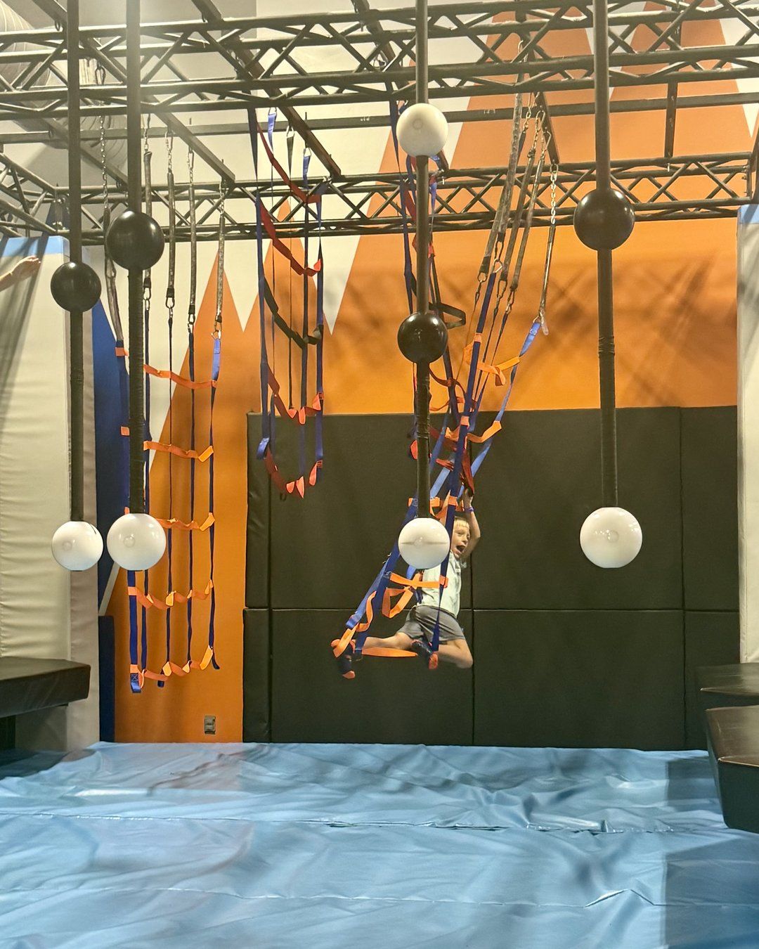 Child swinging on a ninja obstacle course with hanging balls and ladders at Summit Adventure Park